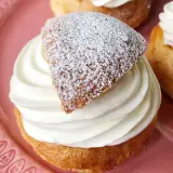 En gammaldags semla med fluffig grädde och pudrat lock på en rosa tallrik.