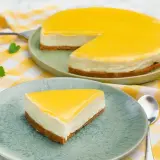 En krämig cheesecake med en syrlig lemon curd-topping, serverad på en ljusgrön tallrik med en gulrutig duk.