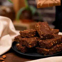 En hög med chokladdoppade dadlar och mandlar på en svart tallrik, omgivna av en ljus duk.
