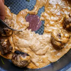 Köttbullar i krämig sås, perfekt tjocknad med maizena istället för potatismjöl. En gaffel rör om i den gyllene såsen.