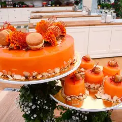 En stor och flera små orangea tårtor med spegelblank glasyr, dekorerade med makroner och blommor.
