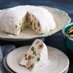 En bit av en vit nougatkaka med nötter och pistagenötter, perfekt att baka med nougat.