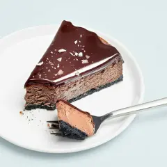 En bit choklad cheesecake med glansig glasyr och flingsalt. En gaffel med en bit av kakan ligger bredvid.