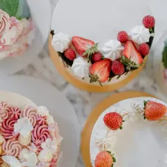 Flera vackra tårtor med fantasifulla dekorationer. En tårta är dekorerad med jordgubbar och maränger, en annan med rosa och vita blommor i frosting. Det är en festlig syn att dekorera tårta!