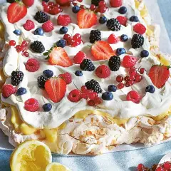 En stor pavlova i långpanna, täckt med vispgrädde, lemon curd och massor av färska bär som jordgubbar, hallon, blåbär och vinbär.