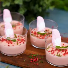 Fyra glas med rosa juleskum pannacotta, toppade med marshmallows, mynta och torkade hallon.
