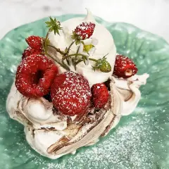 En härlig pavlova choklad med vispgrädde och färska bär, pudrad med florsocker på en grön tallrik.