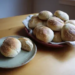 Nybakade bullar med sesamfrön, gjorda med rågsikt istället för vetemjöl. En del ligger i en korg, en annan på en tallrik.