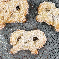 Gyllene kringlor täckta med socker strössel ligger på ett mönstrat underlag. Perfekta till fikat!