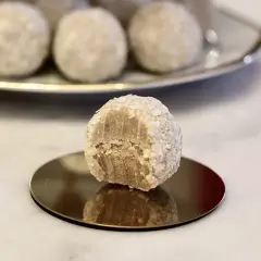 En närbild på en bit av en vit chokladboll, rullad i kokosflingor, med fler chokladbollar i bakgrunden.