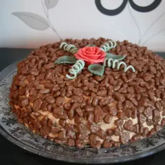 En härlig daim tårta täckt med chokladbitar och dekorerad med en rosa ros och gröna blad.