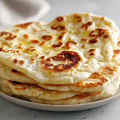 En hög med fluffigt, gyllene naanbröd, perfekt för ditt nästa naan recept. Smält smör glänser på toppen.