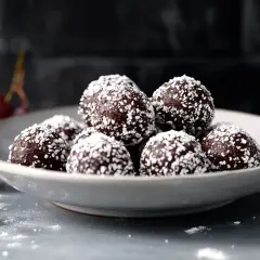 En skål med lyxiga chokladbollar, rullade i kokos. Körsbär ligger bredvid.