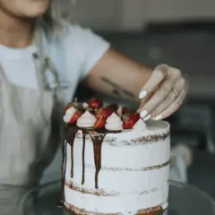 En person dekorerar en tårta med jordgubbar och grädde. Det är en vacker tårta som är redo att spritsa tårta.