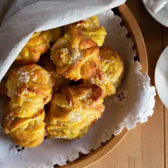 En korg med gyllene saffransbullar med mandelmassa och vanilj, toppade med pärlsocker. En vit duk draperad över bullarna.