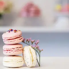 En stapel rosa och vita macarons, dekorerade med blomblad och en liten lila blomma. Perfekt för essenser bakning.