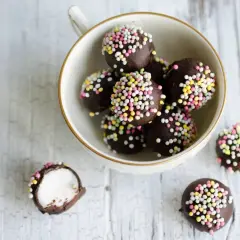 Chokladbollar med färgglatt strössel, perfekta för ett enkelt punschpraliner recept. En är uppskuren och visar ett vitt, fluffigt inre.