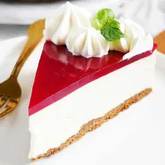 En bit pepparkakscheesecake med vit choklad, toppad med vispgrädde och gelé. En gyllene gaffel ligger bredvid.