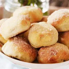 En skål med nybakade bullar, perfekt för att baka med söt jäst. De är pudrade med socker och ser aptitliga ut.