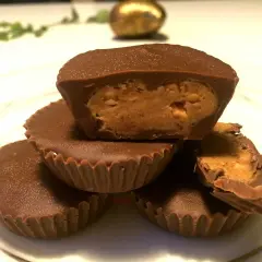 En hög med chokladkoppar med jordnötssmörsfyllning. En är uppskuren och visar den krämiga fyllningen.