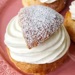 En gammaldags semla med fluffig grädde och pudrat lock på en rosa tallrik.