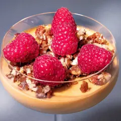 En krämig dulce de leche pannacotta toppad med färska hallon och nötter i ett glas.