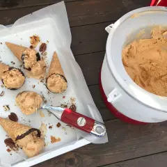 Färdiggjord dulce de leche glass i strutar, toppad med nötter och choklad. En skopa väntar bredvid glassmaskinen.