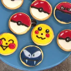Sju dekorerade kakor på en blå tallrik, inklusive Pikachu, Pokémons och en Gastly. En härlig pokemon tårta för alla fans!