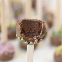 Chokladiga cake pops med färgglada strössel. En är uppäten och visar det saftiga inkråmet.