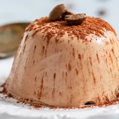 Krämig kaffepanna cotta toppad med kakaopulver och kaffebönor, garnerad med mynta.