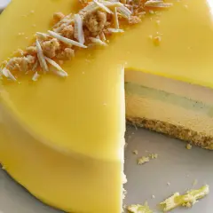 En vacker moussetårta med passionsfrukt, täckt av gul glasyr och toppad med smulor och vit choklad.
