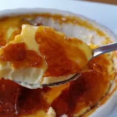En sked lyfter en bit krämig creme brulee cheesecake med karamelliserat sockerlock.