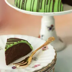 En bit av en himmelsk hallontårta med grön marsipan och chokladdrizzle. En gyllene gaffel ligger på en tallrik med blommor.