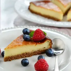 En bit krämig cheesecake med digestivebotten utan ugn, dekorerad med färska bär och mynta.