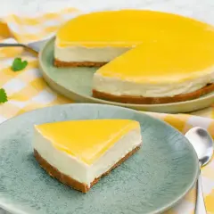 En krämig cheesecake med en syrlig lemon curd-topping, serverad på en ljusgrön tallrik med en gulrutig duk.