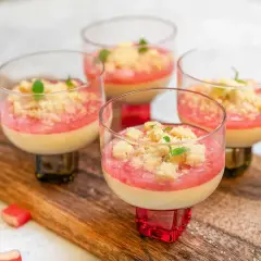 Fyra glas med krämig pannacotta med rabarberkompott och smuldeg. Garnerad med mynta. En härlig sommardessert.