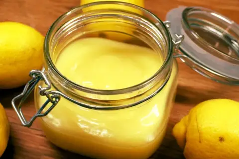 En burk med krämig, solgul lemon curd omgiven av färska citroner. Perfekt för bakning eller som tillbehör.