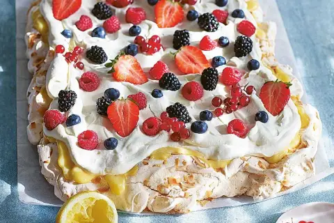 En stor pavlova i långpanna, täckt med vispgrädde, lemon curd och massor av färska bär som jordgubbar, hallon, blåbär och vinbär.