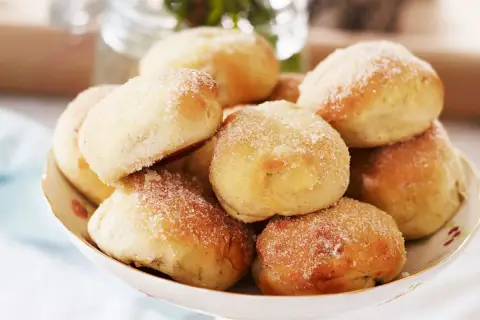 En skål med nybakade bullar, perfekt för att baka med söt jäst. De är pudrade med socker och ser aptitliga ut.
