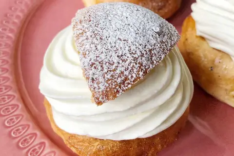 En gammaldags semla med fluffig grädde och pudrat lock på en rosa tallrik.