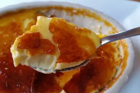 En sked tar en bit av en krämig creme brulee med knäckig karamell.