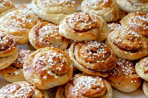 En hög med gyllene kanelbullar, toppade med pärlsocker. Perfekt för fikat, här är ett enkelt kanelbullar recept.