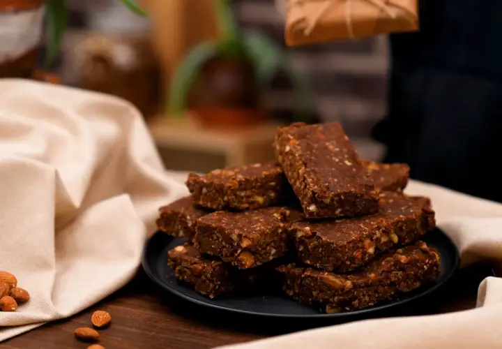 En hög med chokladdoppade dadlar och mandlar på en svart tallrik, omgivna av en ljus duk.