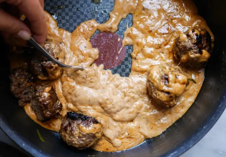 Köttbullar i krämig sås, perfekt tjocknad med maizena istället för potatismjöl. En gaffel rör om i den gyllene såsen.
