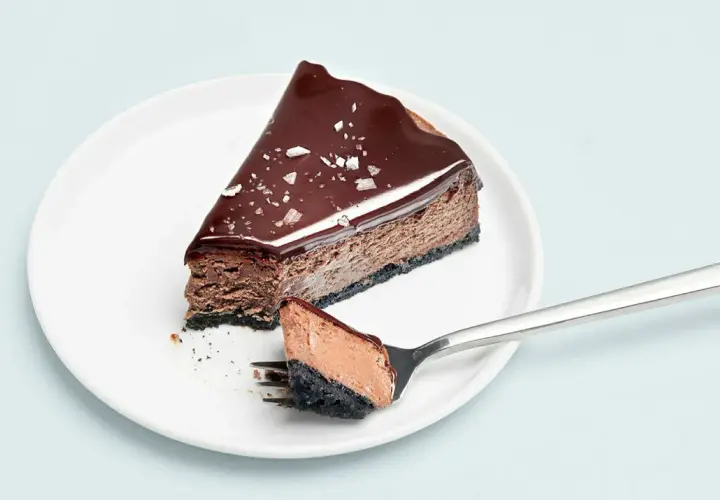 En bit choklad cheesecake med glansig glasyr och flingsalt. En gaffel med en bit av kakan ligger bredvid.