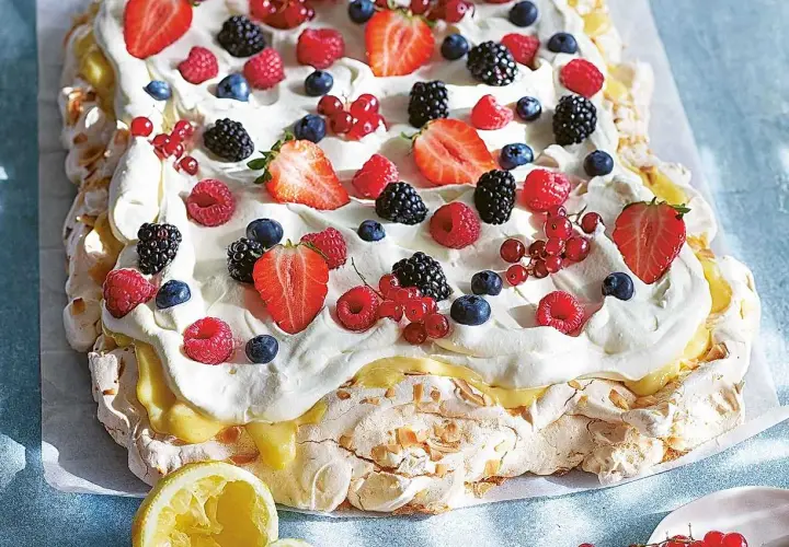 En stor pavlova i långpanna, täckt med vispgrädde, lemon curd och massor av färska bär som jordgubbar, hallon, blåbär och vinbär.