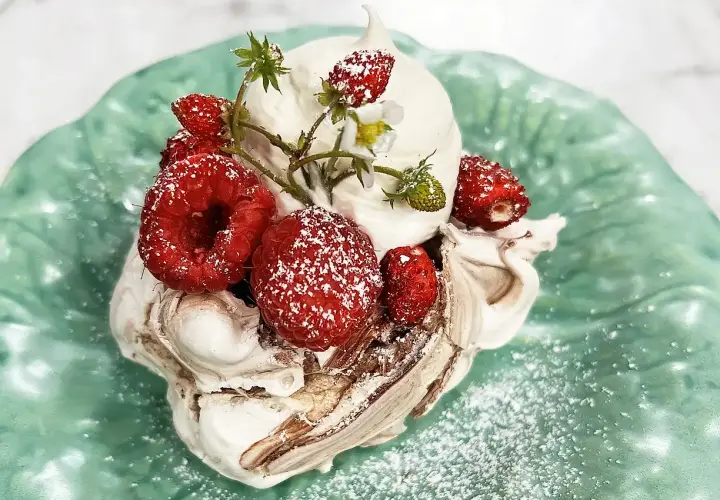 En härlig pavlova choklad med vispgrädde och färska bär, pudrad med florsocker på en grön tallrik.