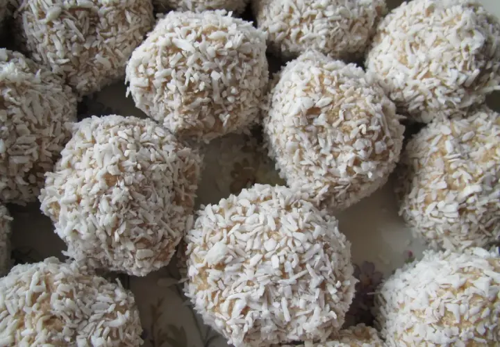 En hög med ljusa havrebollar täckta av kokosflingor. De ser ut att vara redo att ätas!
