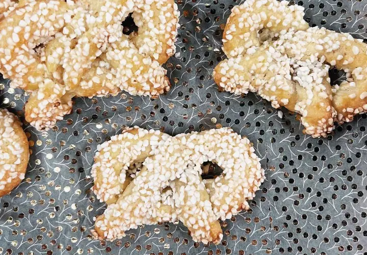 Gyllene kringlor täckta med socker strössel ligger på ett mönstrat underlag. Perfekta till fikat!