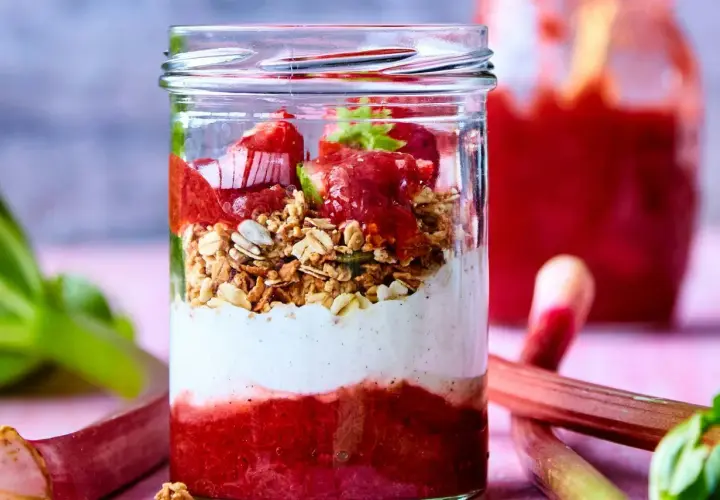 En glasburk med lager av rabarberkompott, yoghurt och granola. Rabarber är giftiga efter midsommar, men denna dessert är säker att njuta av.